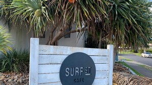 Un panneau en bois sur lequel est écrit « SURF ST CAFE », entouré de rochers et de plantes.