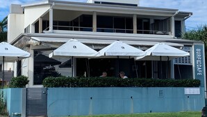 Un bâtiment moderne doté d’un toit plat, de grandes fenêtres et d’une enseigne indiquant « SURFCAFE ».