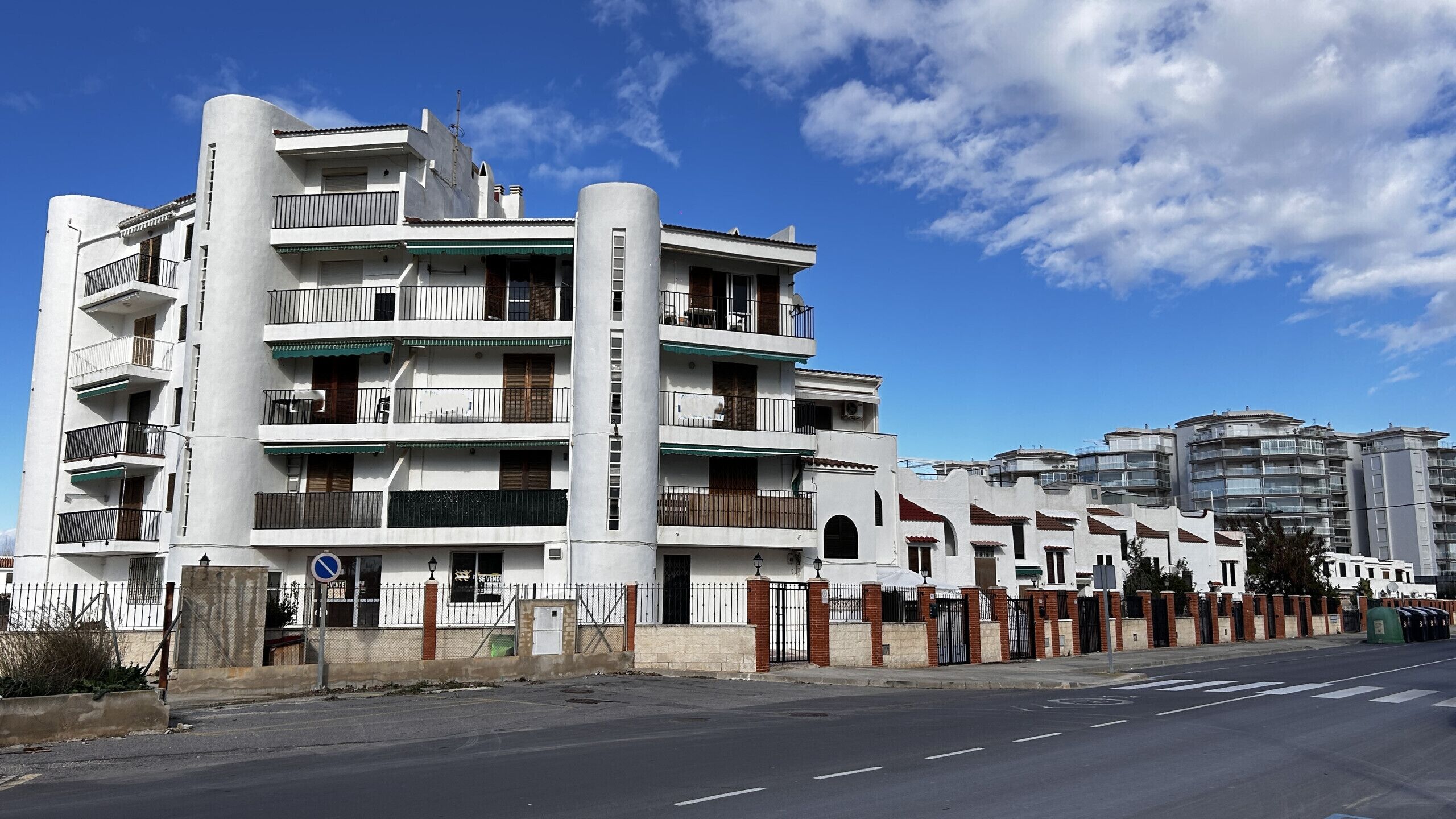 Un edificio residencial de varios pisos con balcones, entrada protegida por un portón y cielo despejado.