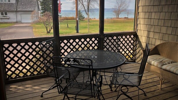 Un espacio al aire libre cubierto con una mesa y sillas, un sofá de mimbre y vistas a una casa y árboles.
