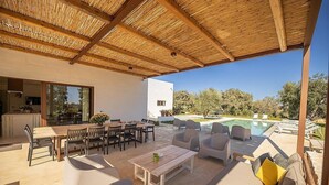 Une terrasse extérieure dotée d’un plafond en bois, d’une piscine et d’un espace repas avec des tables et des chaises.