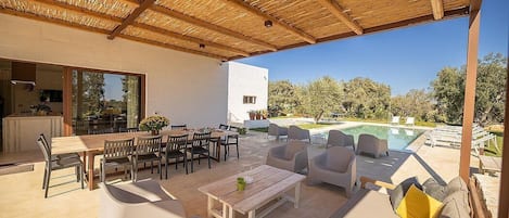 An outdoor patio with a wooden ceiling, a pool, and a dining area with tables and chairs.