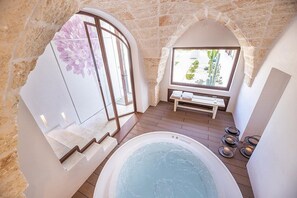 Ein Wellnessbereich mit Whirlpool, Steinwänden und einer Bank an einem Fenster mit Blick auf einen Garten.