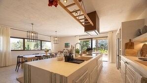 Une cuisine spacieuse dotée d’un grand îlot central, d’appareils électroménagers modernes et bénéficiant d’un éclairage naturel abondant grâce à de grandes fenêtres.