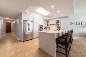 A modern kitchen with a central island, stainless steel appliances, and a bar seating area. - Two Bedroom Condo with Views of Gulf, Bay, and Outdoor Pool Decks! (Orange Beach)