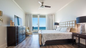 Une chambre d’hôtel avec un lit, une commode, une chaise et une vue sur l’océan, visible à travers les portes coulissantes.