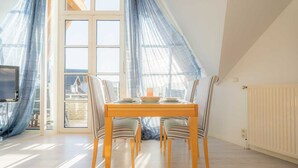 Un coin repas avec une table et des chaises, de grandes fenêtres ornées de rideaux légers et une vue sur l’extérieur.