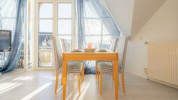 Ein Essbereich mit Tisch und Stühlen, große Fenster mit durchsichtigen Vorhängen und Blick ins Freie.