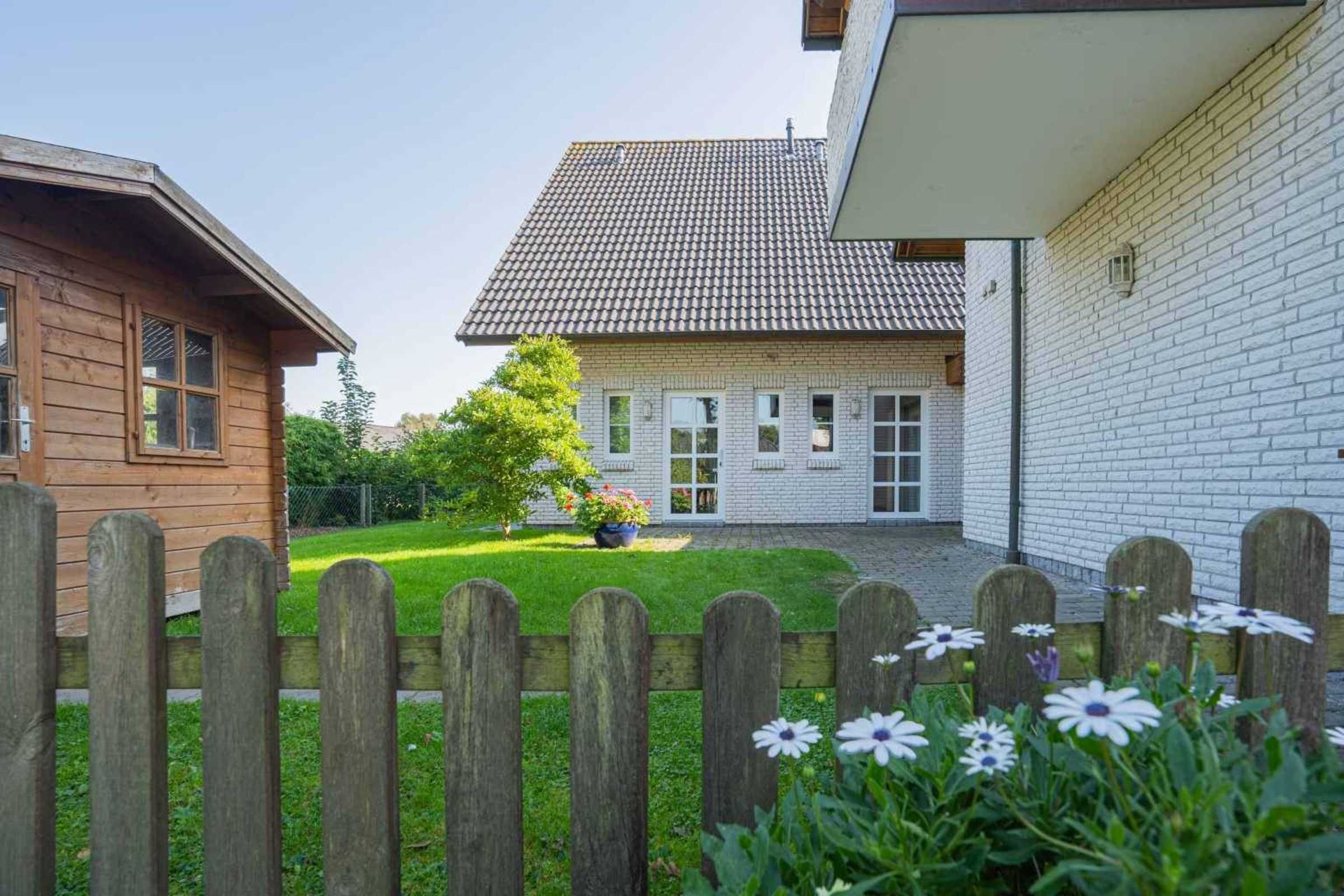 Ein zweistöckiges Haus mit Ziegeldach, Holzzaun und einem Garten mit Blumen.