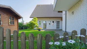Ein zweistöckiges Haus mit Ziegeldach, Holzzaun und einem Garten mit Blumen.