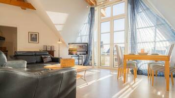 Ein modernes Wohnzimmer mit einer schwarzen Ledersofa, einem Holzespeisetisch mit Stühlen und einem großen Fenster mit blauen Vorhängen.