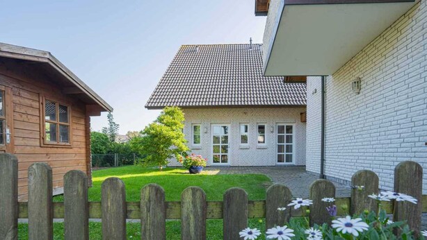 Une maison à deux étages, avec un toit en tuiles, une clôture en bois et un jardin fleuri.