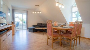Une cuisine moderne avec des meubles en bois, un coin repas doté d’une table ronde et de chaises, et une grande fenêtre laissant entrer la lumière naturelle.
