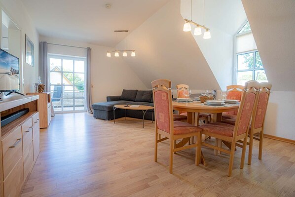 A modern kitchen with wooden cabinets, a dining area with a round table and chairs, and a large window providing natural light.