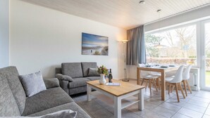 Uma sala de estar moderna com um sofá cinzento, uma mesa de centro de madeira e uma área de jantar com mesa e cadeiras.