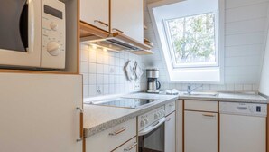 Cozinha moderna com armários brancos, forno embutido, micro-ondas, máquina de café e janela que proporciona luz natural.
