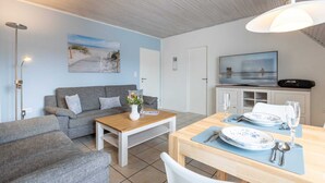 Uma sala de estar moderna com sofá, mesa de centro e mesa de jantar posta para dois.