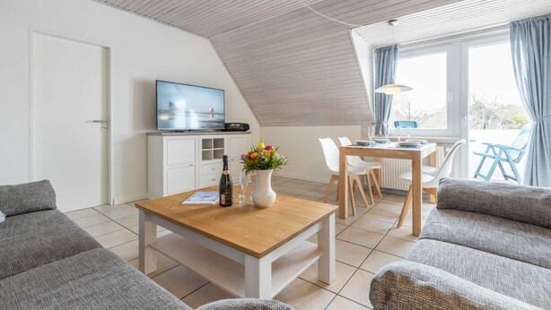 Uma sala de estar moderna com uma mesa de jantar de madeira, sofás cinzas, uma televisão e uma área de cozinha.