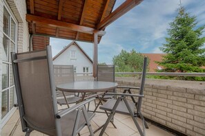 Eine überdachte Terrasse im Freien mit einem runden Tisch und Stühlen, einer Backsteinmauer und einem Blick auf ein Haus und Bäume im Hintergrund.