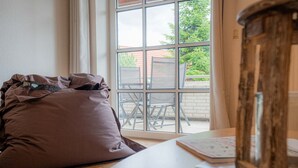 A room with a large window, a wooden table, and a brown cushion. - House Zur Sonnenseite - Apartment 3 Irmi (ID 415) (Garding, Kirchspiel)