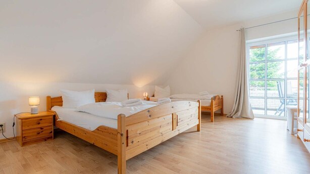 A bedroom with a wooden bed, bedside tables, and a large window with curtains. - House Zur Sonnenseite - Apartment 3 Irmi (ID 415) (Garding, Kirchspiel)