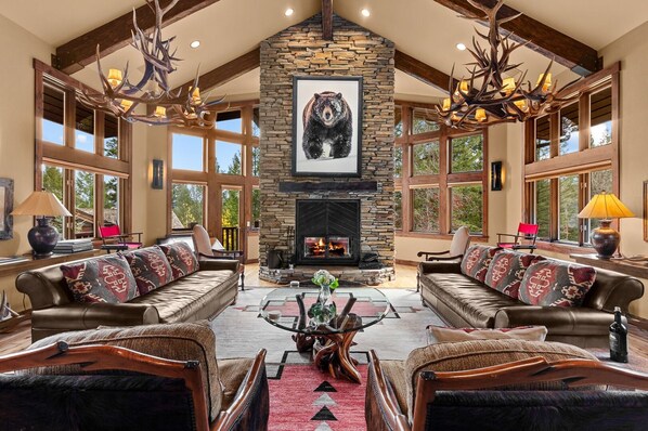 A spacious living room with a stone fireplace, leather sofas, and large windows.
