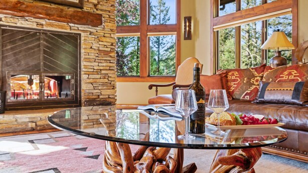 A cozy living room with a stone fireplace, a glass coffee table with a wooden base, and a sofa with patterned cushions. - RMR: Sundance Ski Lodge | Luxury Ski - In / Ski - Out (Teton Village)