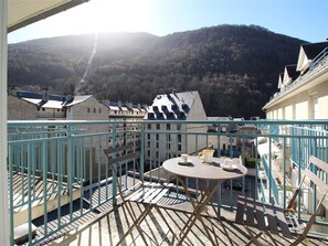 A balcony with a table, chairs, and a view of a mountainous landscape.