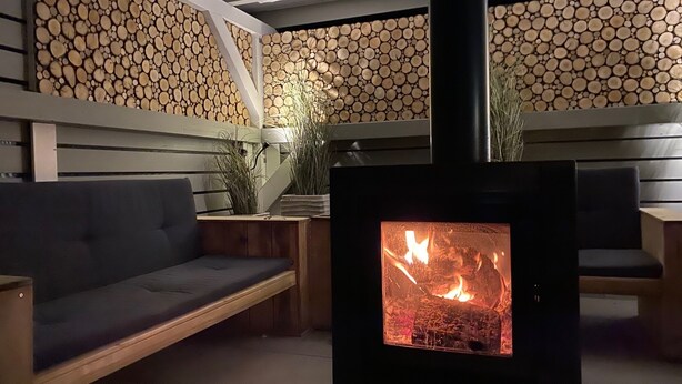 Une pièce chaleureuse avec un poêle à bois encastré, un canapé et un mur en bois recouvert de rondins.