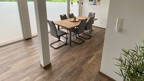 Un espace repas moderne avec une table et des chaises en bois, de grandes fenêtres offrant une vue sur un lac et la verdure, et un luminaire suspendu.