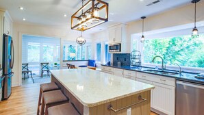 Une cuisine moderne dotée d  ’un grand îlot central, d’appareils électroménagers en acier inoxydable et offrant une vue sur la verdure environnante.