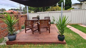 Una terraza de madera con una mesa y sillas, rodeada por un muro de ladrillo y una valla blanca.