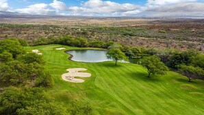A golf course with a pond, surrounded by greenery and distant mountains.