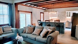 Ein Wohnzimmer mit einer Couch, einem Couchtisch mit Blumen und einer Küchenzeile mit Esstisch und Stühlen.