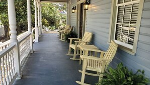 Eine Veranda mit Holzschaukelstühlen und Tischen, einem weißen Geländer und einem Fenster mit Fensterläden.