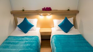 Ein Doppelzimmer mit zwei Betten, jeweils mit blauer Bettdecke und Kissen, einem Holzkopfende und einer kleinen Ablage mit Dekorationen.