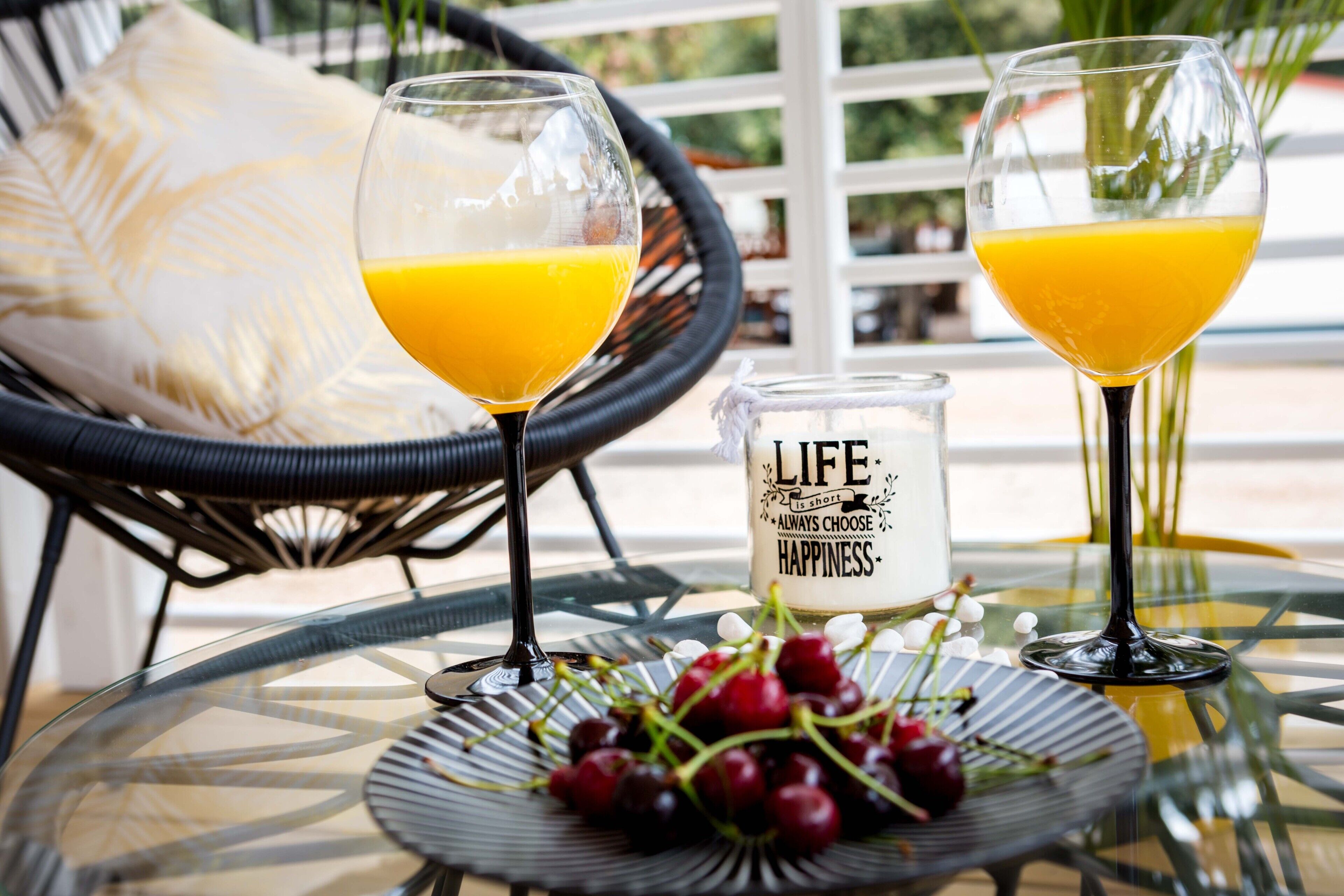 Two glasses of orange juice on a glass table with a candle and grapes.