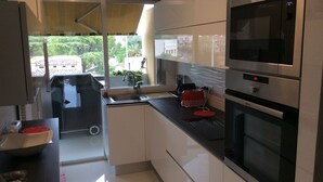 A modern kitchen with stainless steel appliances, a built-in oven, and a window with a view of greenery. - Rare gem, rooftop villa, 150m2 living space on park, janitor air-conditioning, pisc, pkg, (Cannes)