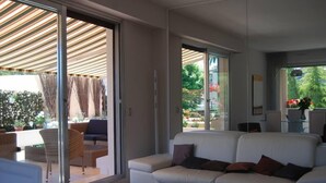 A modern living room with a white sofa, a glass coffee table, and a sliding glass door leading to an outdoor patio area. - Rare gem, rooftop villa, 150m2 living space on park, janitor air-conditioning, pisc, pkg, (Cannes)