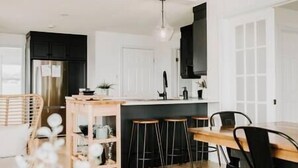 A modern kitchen with a central island, bar stools, and a dining table. - Oakes House+waterfront+games room+hot tub+Firepit (Charlo)