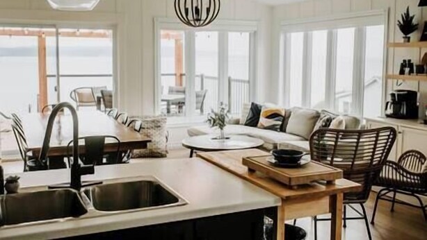 A modern kitchen with a central island, a dining area with a round table, and a seating arrangement with chairs. - Oakes House+waterfront+games room+hot tub+Firepit (Charlo)