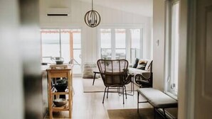 A modern living room with a wooden floor, a dining area with a table and chairs, and a large window providing natural light. - Oakes House+waterfront+games room+hot tub+Firepit (Charlo)