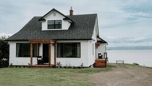 A white house with a dark roof, large windows, and a wooden porch. - Oakes House+waterfront+games room+hot tub+Firepit (Charlo)