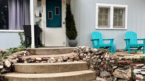 Uma casa com porta azul, escadaria de pedra e duas cadeiras Adirondack turquesa na varanda.