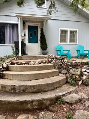 Une maison avec une porte bleue, un escalier en pierre et deux fauteuils Adirondack turquoise à l’extérieur.
