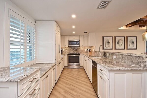 A modern kitchen with white cabinetry, granite countertops, a built-in oven, and a microwave. - Luxury On The Beach in the Heart of Siesta Key at Crystal Sands 809 (Siesta Key)