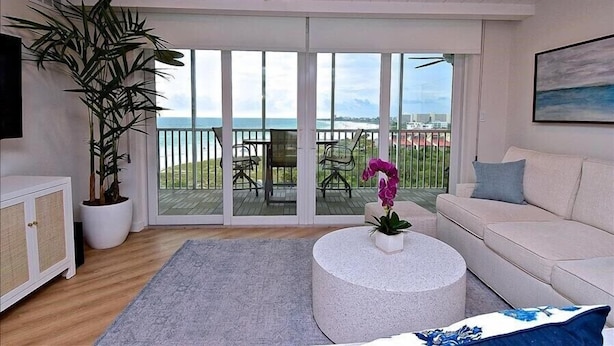 Een moderne woonkamer met een grote schuifpui die uitkomt op een balkon met uitzicht op de oceaan.