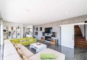 A modern living room with a sofa, coffee table, TV, fireplace, and a staircase.