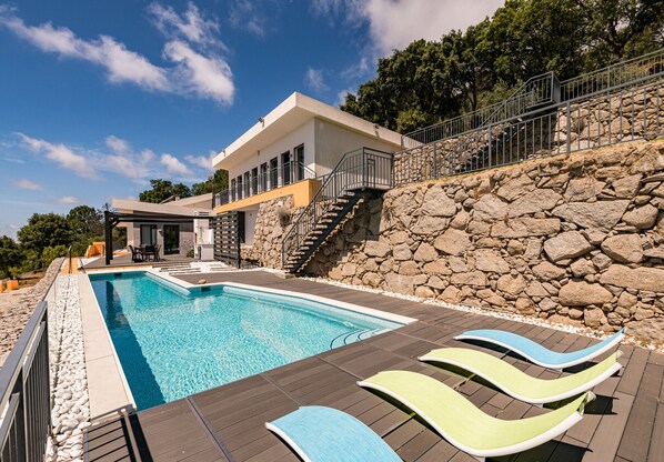 Una piscina con sdraio, un muro in pietra e un edificio con un balcone.
