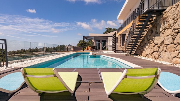 Una piscina con lettini, un muro in pietra e una scala che conduce a un balcone.